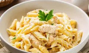 Penne z kremowym sosem i kawałkami kurczaka, posypane parmezanem i udekorowane natką pietruszki. Pyszny makaron z kurczakiem.