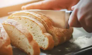Ręka kroi świeży chleb na kromki. Dowiedz się, jak odświeżyć chleb, by znów był pyszny.