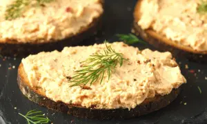 Pyszna pasta z łososia na ciemnym pieczywie, udekorowana gałązką koperku. Idealna na śniadanie lub przekąskę.