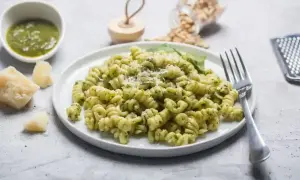 Pyszny makaron z pesto, posypany parmezanem, obok kawałki sera i miseczka sosu. Idealny posiłek dla miłośników włoskich smaków.