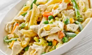 Pyszny makaron z warzywami: penne, kawałki kurczaka, groszek, marchewka, fasolka szparagowa i kukurydza w kremowym sosie.