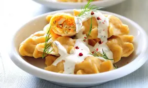 Pyszne, szybkie dania bezmięsne na obiad: pierogi z farszem warzywnym, polane sosem jogurtowym z koperkiem i posypane pieprzem.