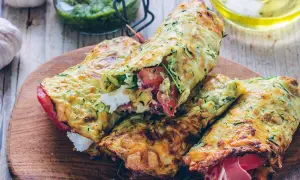 Złociste tortilla z cukinii, nadziewane pomidorami, fetą i szynką, prezentowane na drewnianej desce.