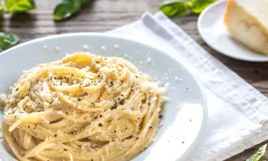 Szybki obiad z makaronem: spaghetti posypane parmezanem i pieprzem, obok kawałek sera i listki bazylii.