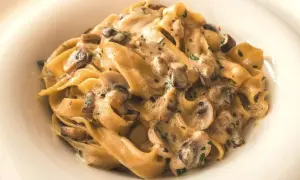 Pappardelle z kremowym sosem i kawałkami pieczarek, posypane natką pietruszki. Pyszny makaron z pieczarkami w białym talerzu.