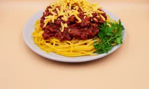 Pyszne spaghetti z mięsem mielonym, posypane żółtym serem i udekorowane gałązką natki pietruszki.