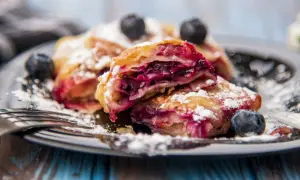 Pyszne ciasto francuskie z borówkami, posypane cukrem pudrem, na talerzu z widelcem.