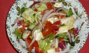 Pyszna sałatka z mix sałat, pomidorów, ogórka, czerwonej cebuli i sera feta, podana na ozdobnym talerzu.
