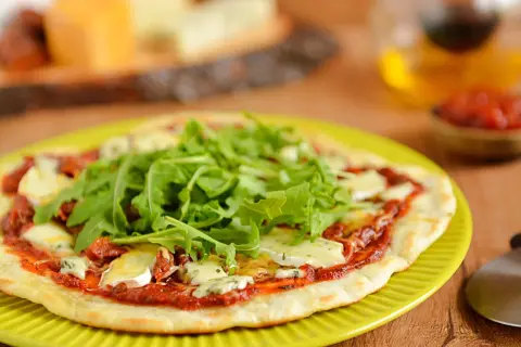 Pyszna pizza z patelni z rukolą i serem pleśniowym, podana na zielonym talerzu.