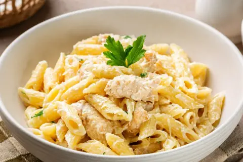 Penne z kremowym sosem i kawałkami kurczaka, posypane parmezanem i udekorowane natką pietruszki. Pyszny makaron z kurczakiem.