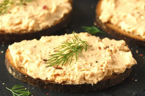 Pyszna pasta z łososia na ciemnym pieczywie, udekorowana gałązką koperku. Idealna na śniadanie lub przekąskę.