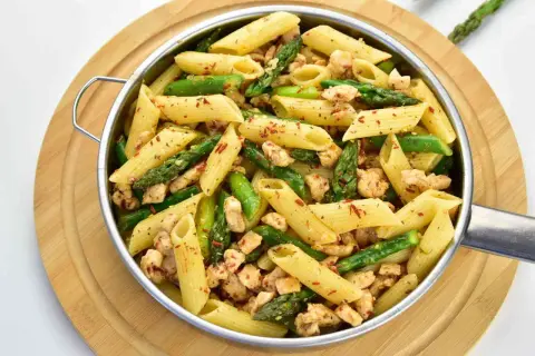 Penne z kurczakiem i szparagami, posypane papryką. Pyszne danie na obiad.
