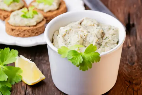 Pyszna pasta z makreli i jajek, podana w białej miseczce, z dodatkiem cytryny i natki pietruszki. Idealna na kanapki.