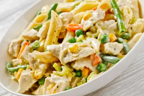 Pyszny makaron z warzywami: penne, kawałki kurczaka, groszek, marchewka, fasolka szparagowa i kukurydza w kremowym sosie.