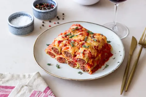 Pyszne cannelloni z mięsem mielonym, zapieczone pod sosem pomidorowym i serem, ozdobione świeżym tymiankiem.