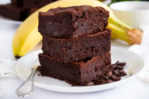 Stos puszystych brownie z bananami, ozdobiony ziarnami kawy, na talerzu z bananem w tle.