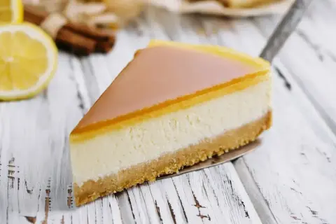 Pyszny sernik z mascarpone na kruchym spodzie, z delikatną galaretką na wierzchu. Obok cytryna i laski cynamonu.