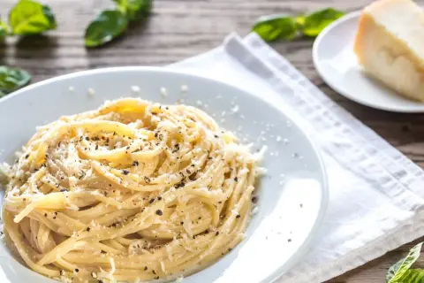 Szybki obiad z makaronem: spaghetti posypane parmezanem i pieprzem, obok kawałek sera i listki bazylii.