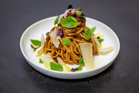 Pyszne spaghetti alla norma z sosem pomidorowym, bakłażanem, bazylią i płatkami parmezanu.