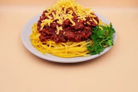 Pyszne spaghetti z mięsem mielonym, posypane żółtym serem i udekorowane gałązką natki pietruszki.