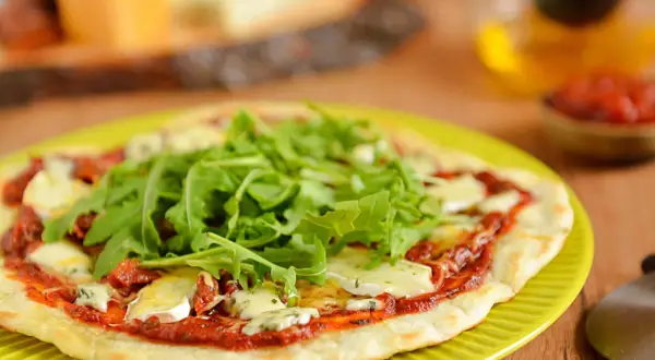 Pyszna pizza z patelni z rukolą i serem pleśniowym, podana na zielonym talerzu.