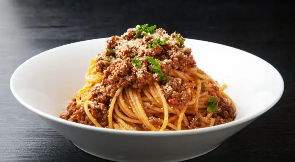 Pyszne spaghetti z bogatym sosem bolognese, posypane parmezanem i natką pietruszki. Idealne danie z makaronem z mięsem mielonym.