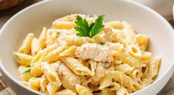 Penne z kremowym sosem i kawałkami kurczaka, posypane parmezanem i udekorowane natką pietruszki. Pyszny makaron z kurczakiem.