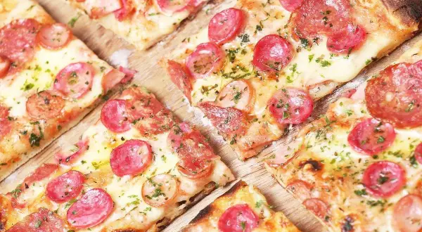 Kawałki pizzy z kiełbasą i serem, idealne na szybki przepis na ciasto do pizzy.