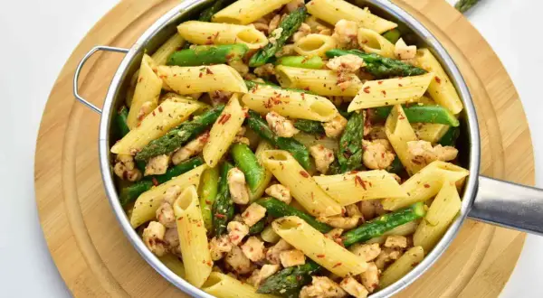 Penne z kurczakiem i szparagami, posypane papryką. Pyszne danie na obiad.