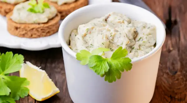 Pyszna pasta z makreli i jajek, podana w białej miseczce, z dodatkiem cytryny i natki pietruszki. Idealna na kanapki.