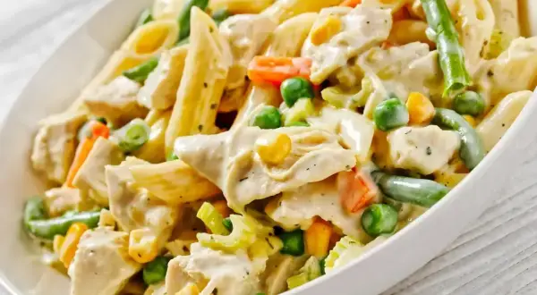 Pyszny makaron z warzywami: penne, kawałki kurczaka, groszek, marchewka, fasolka szparagowa i kukurydza w kremowym sosie.