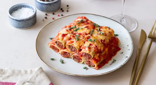 Pyszne cannelloni z mięsem mielonym, zapieczone pod sosem pomidorowym i serem, ozdobione świeżym tymiankiem.