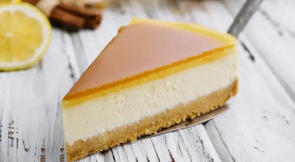 Pyszny sernik z mascarpone na kruchym spodzie, z delikatną galaretką na wierzchu. Obok cytryna i laski cynamonu.