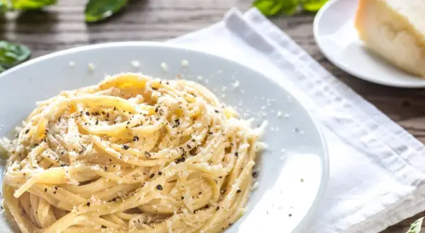 Szybki obiad z makaronem: spaghetti posypane parmezanem i pieprzem, obok kawałek sera i listki bazylii.