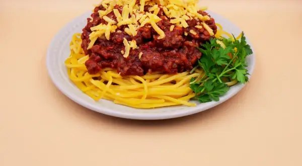 Pyszne spaghetti z mięsem mielonym, posypane żółtym serem i udekorowane gałązką natki pietruszki.