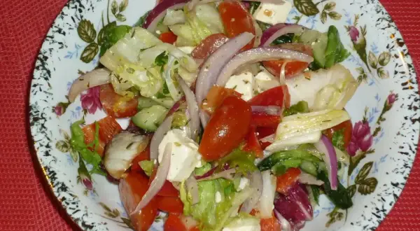 Pyszna sałatka z mix sałat, pomidorów, ogórka, czerwonej cebuli i sera feta, podana na ozdobnym talerzu.