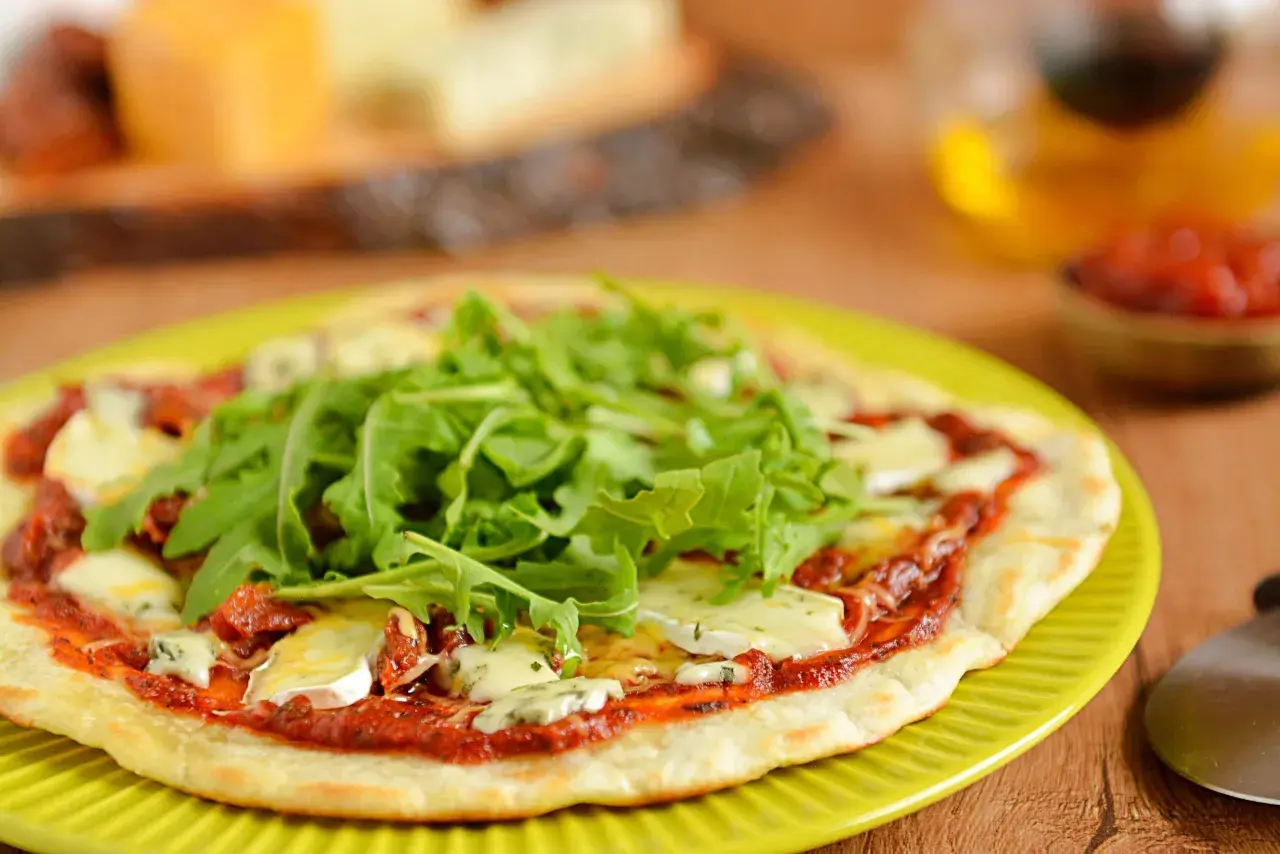 Pyszna pizza z patelni z rukolą i serem pleśniowym, podana na zielonym talerzu.