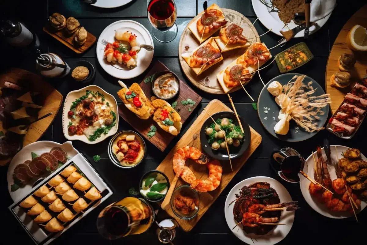 Tapas co to? Kolorowy stół pełen przekąsek: krewetki, pieczywo, ser, oliwki i inne smakołyki. Idealne na spotkanie.