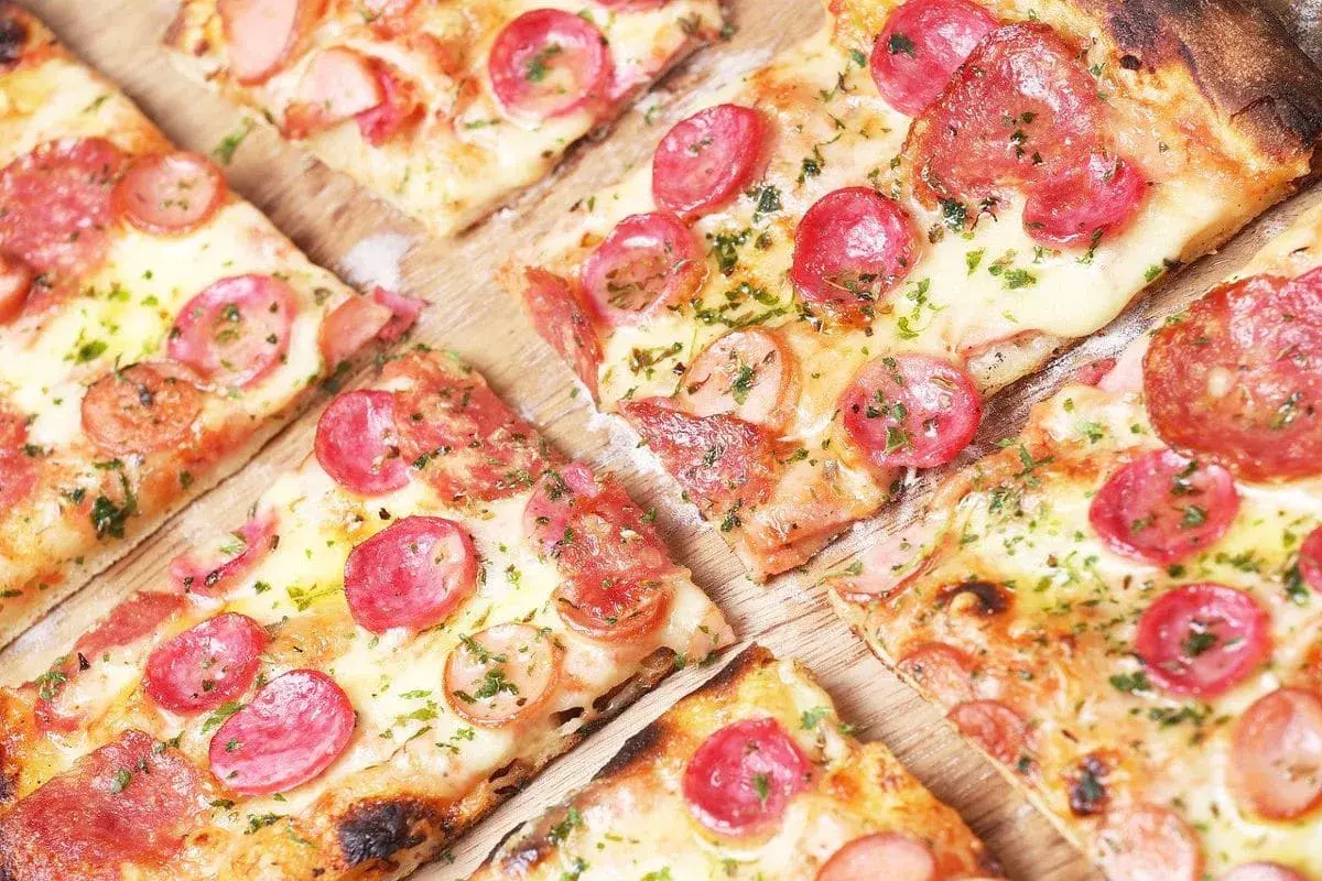 Kawałki pizzy z kiełbasą i serem, idealne na szybki przepis na ciasto do pizzy.