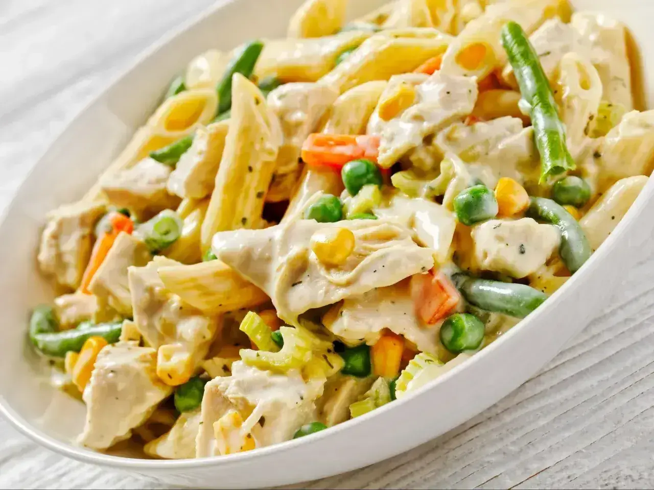 Pyszny makaron z warzywami: penne, kawałki kurczaka, groszek, marchewka, fasolka szparagowa i kukurydza w kremowym sosie.