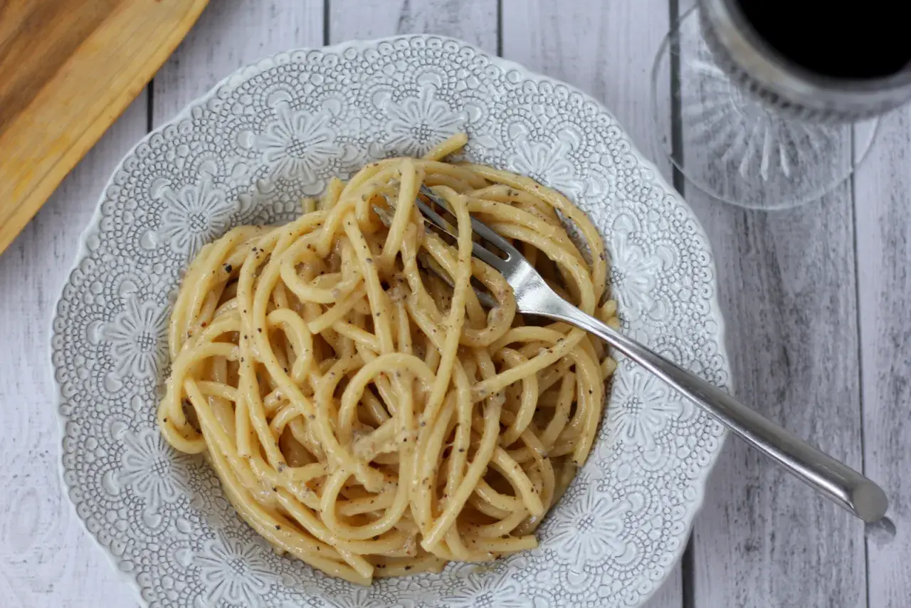 Porcja kremowego cacio e pepe z widelcem w talerzu, gotowa do zjedzenia.