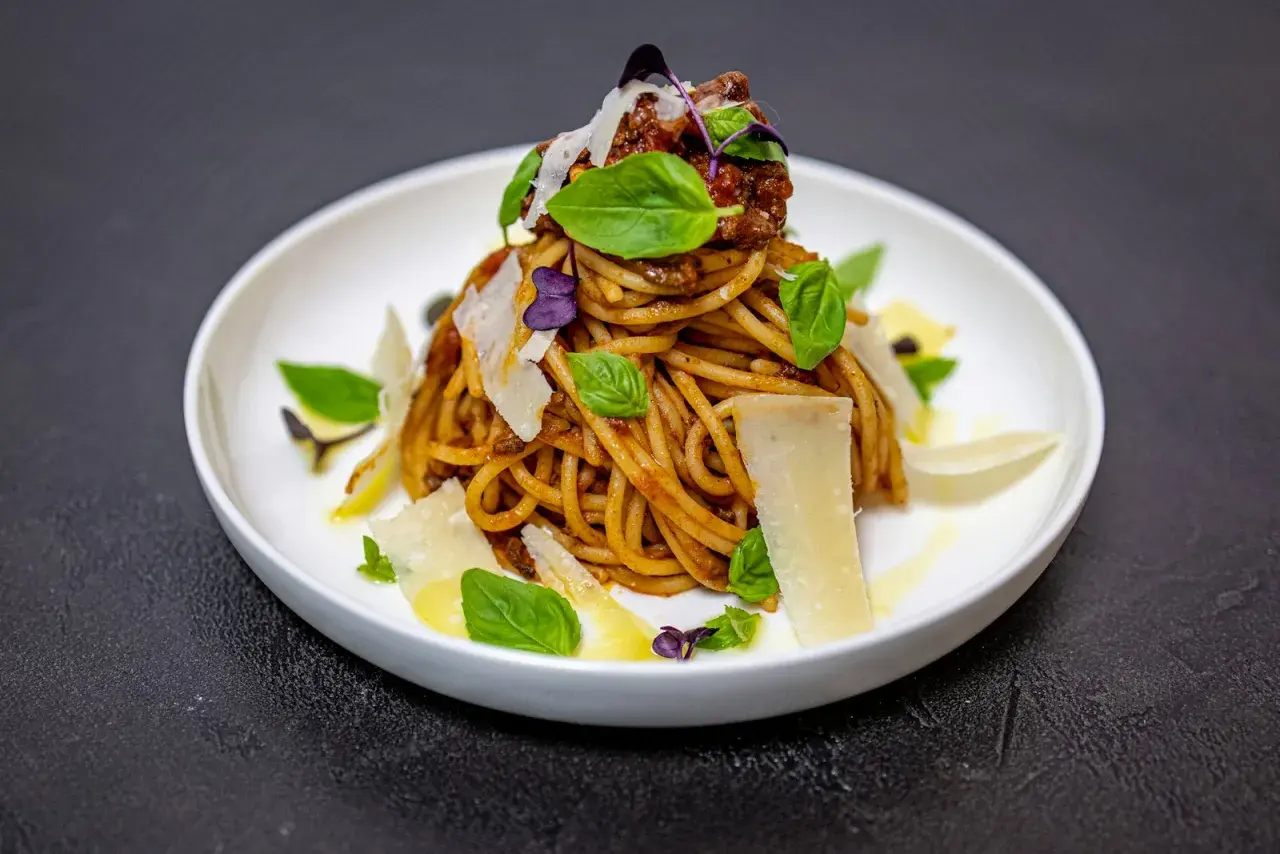 Pyszne spaghetti alla norma z sosem pomidorowym, bakłażanem, bazylią i płatkami parmezanu.