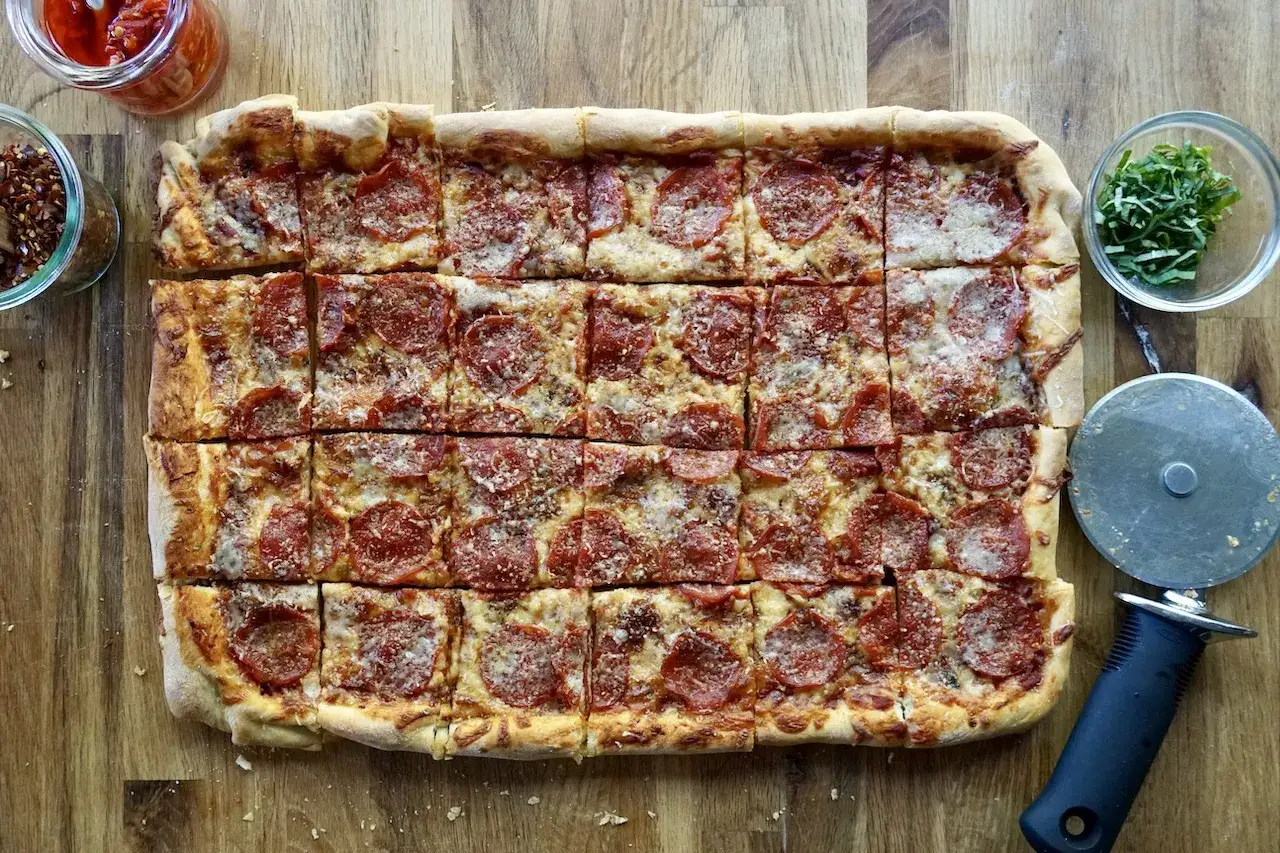 Domowa pizza na blachę z pepperoni, posypana parmezanem. Idealna na rodzinne spotkanie, według prostego przepisu.