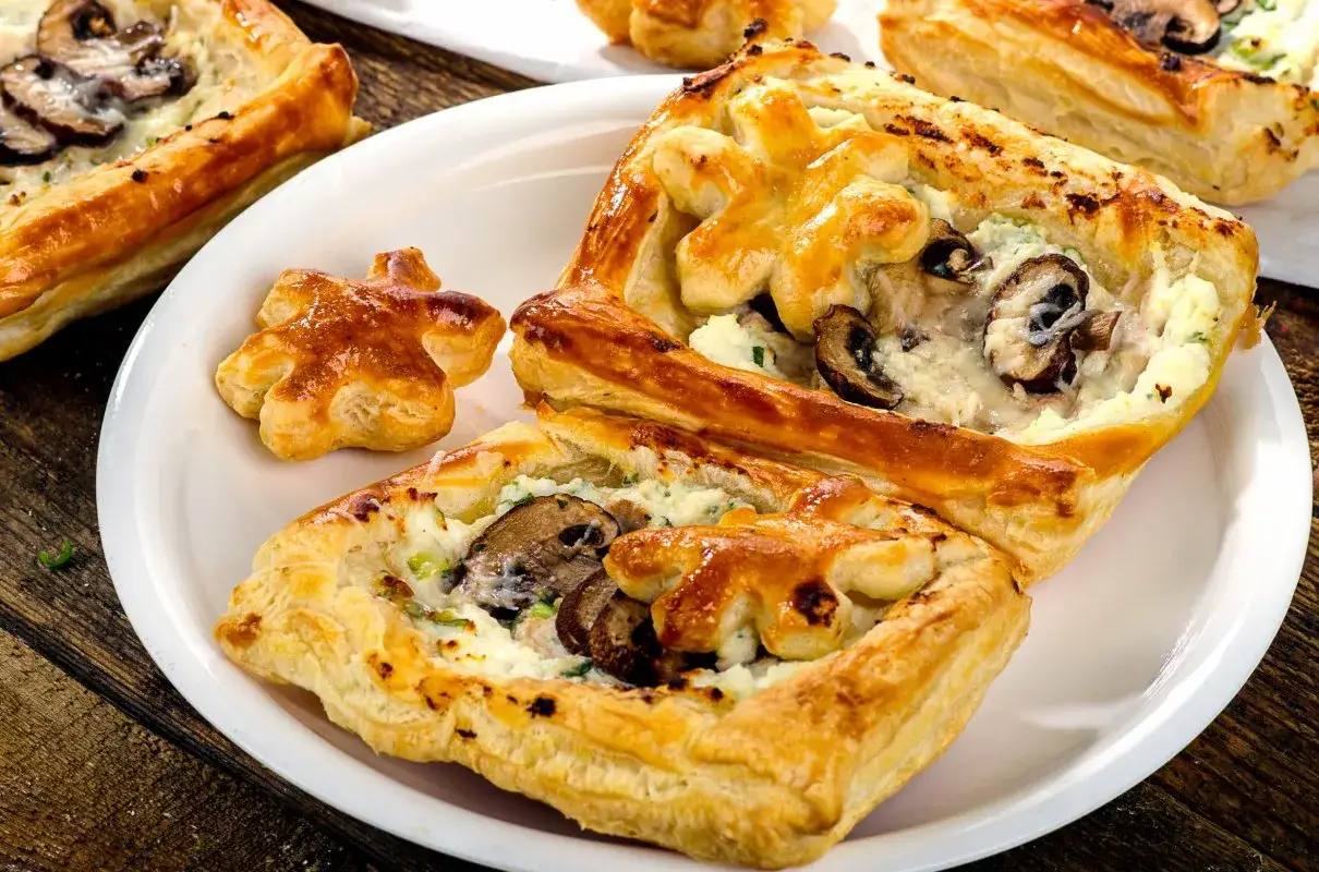 Chrupiące ciasto francuskie z pieczarkami i serem, podane na białym talerzu. Idealna przekąska.