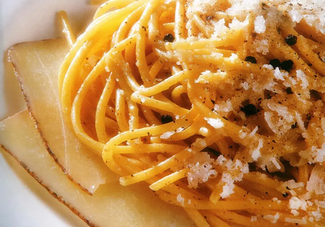 Pyszne spaghetti cacio e pepe z tartym serem i czarnym pieprzem, obok plastrów sera.