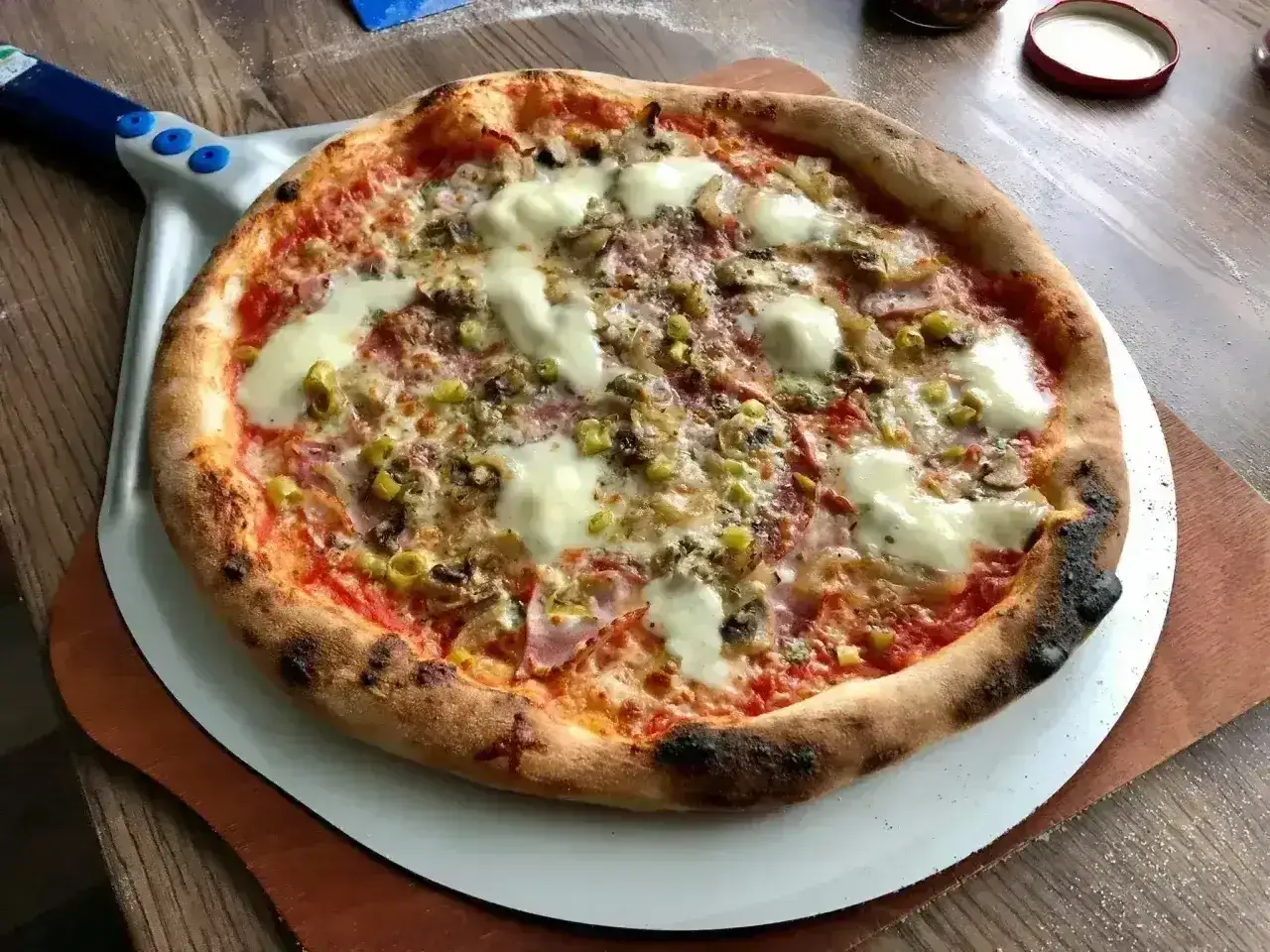 Pyszna pizza na cienkim cieście z serem, pieczarkami i oliwkami, gotowa do podania na łopacie.