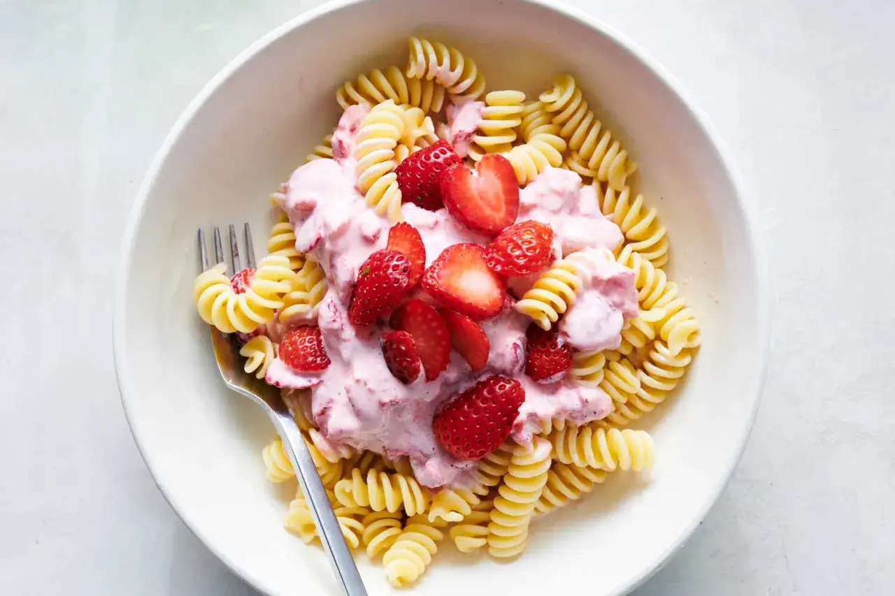 Fusilli z kremowym sosem i świeżymi truskawkami. Pyszny makaron z truskawkami w białej misce, gotowy do zjedzenia.