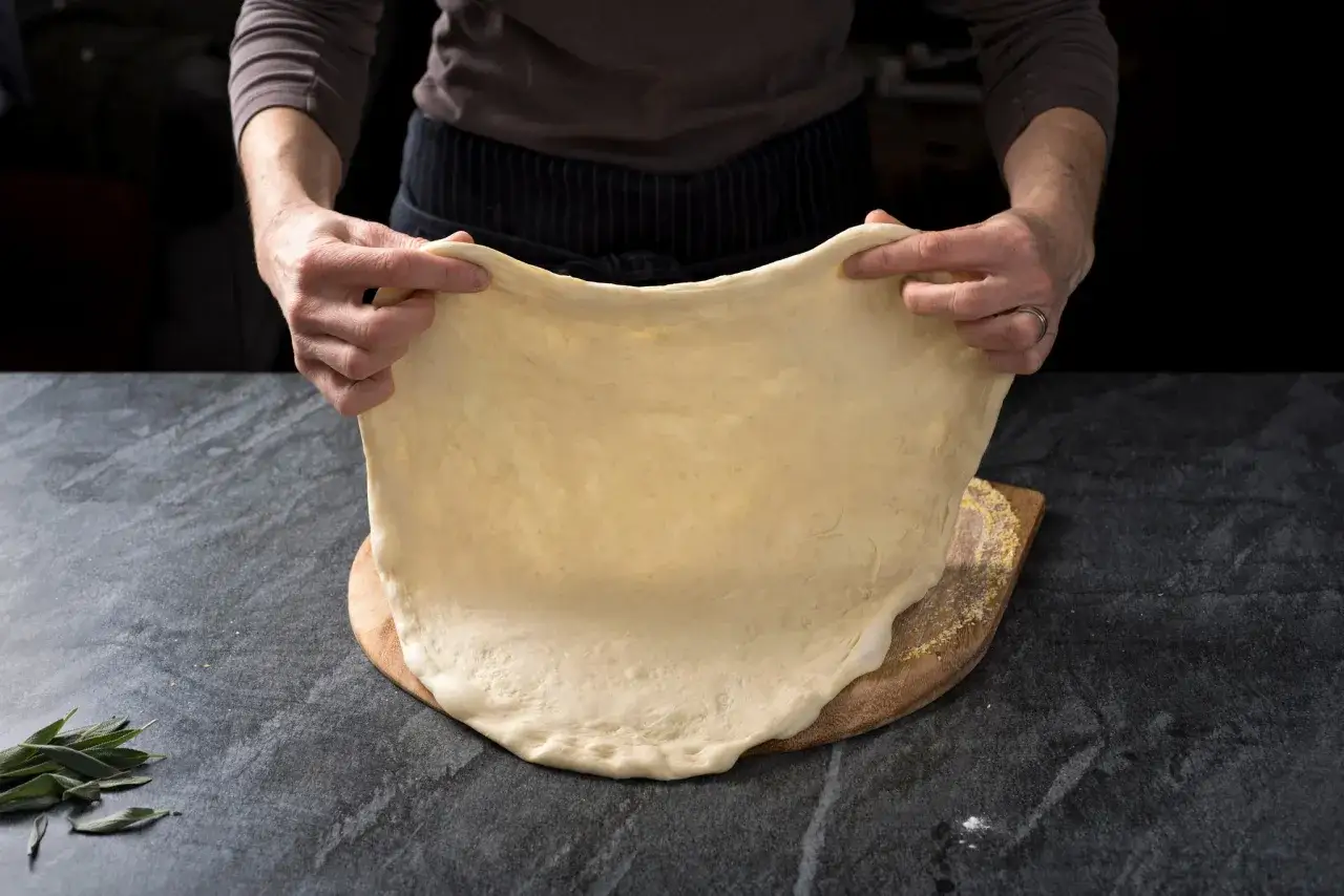 Ręce rozciągają elastyczne ciasto na pizzę, idealne do szybkiego przepisu na ciasto do pizzy.