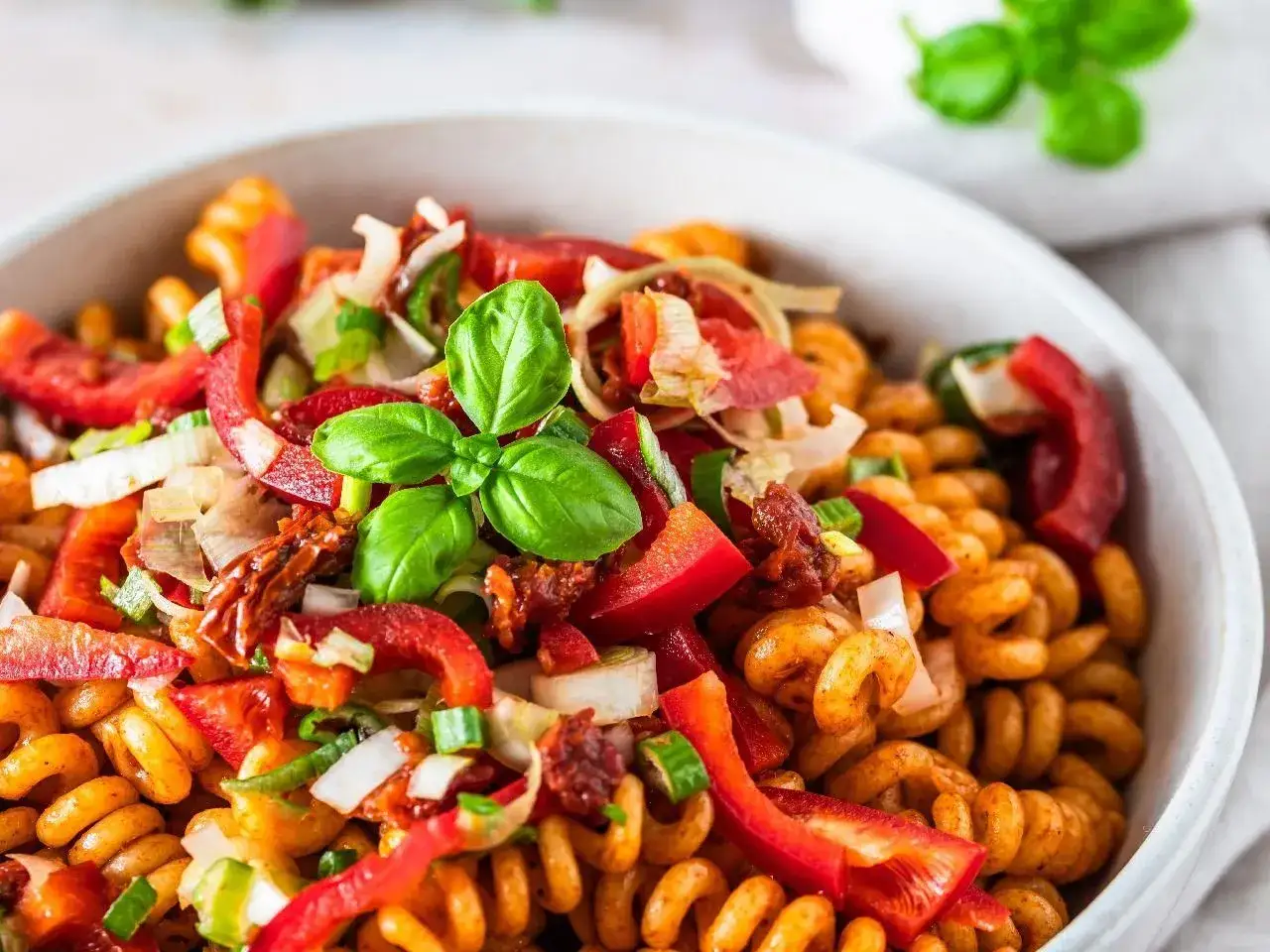 Kolorowa sałatka z makaronem fusilli, papryką, suszonymi pomidorami i świeżą bazylią. Pyszne danie na lato.