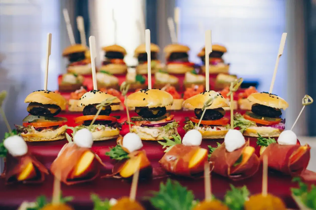 Mini burgery i inne pyszne przekąski na imprezę, ułożone na czerwonym tle.